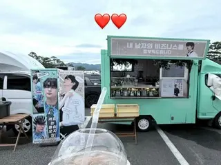 Aktor Byeon WooSeok membuat sepasang hati sambil memegang minuman sebagai hadiah dari mobil kafe